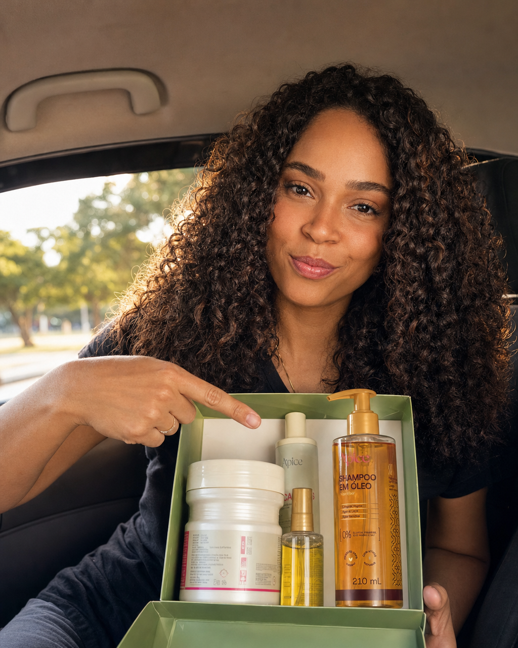 Mulher cacheada no banco do carro segurando uma caixa verde com o Shampoo em Óleo em destaque